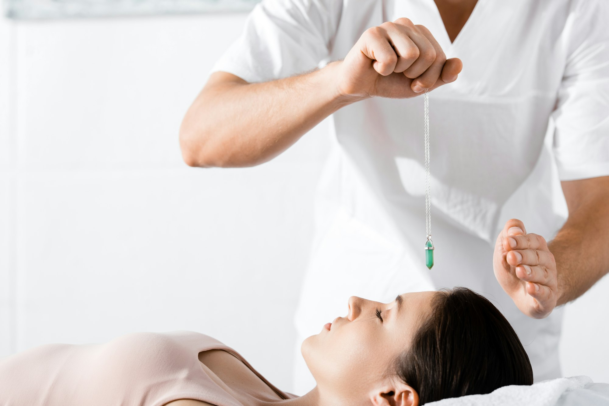 cropped view of hypnotist standing near woman and holding green stone above her face